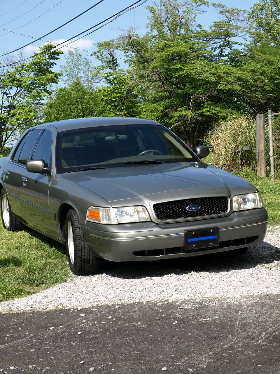Sage-green Ford Crown Victoria with black grille and alloy wheels parked on gravel