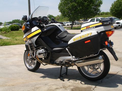 1999 Ford Crown Victoria - A police motorcycle is parked on a concrete surface, with other vehicles visible in the background.