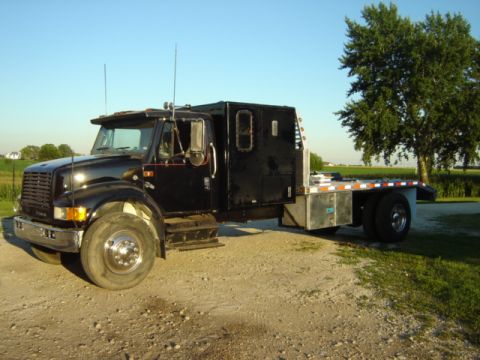 1992 Ford Bronco - This flatbed truck has a custom sleeper cab and is parked on a dirt road with a tree in the background.
