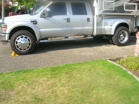 2008 Ford F-450 - A silver Ford F-450 pickup truck is parked on a driveway, equipped with a camper shell for extended travel.