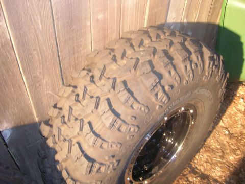 1996 Ford Bronco - Close-up of an off-road tire and rim against a wooden fence.