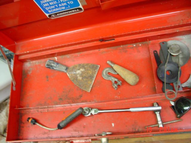 Open red toolbox with a rusty putty knife, a hook, a wooden-handled tool, a socket wrench, and other metal parts