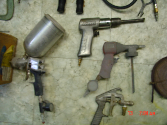 Several air-powered tools including a spray gun, a hammer, and a rivet gun are laid out on a floor