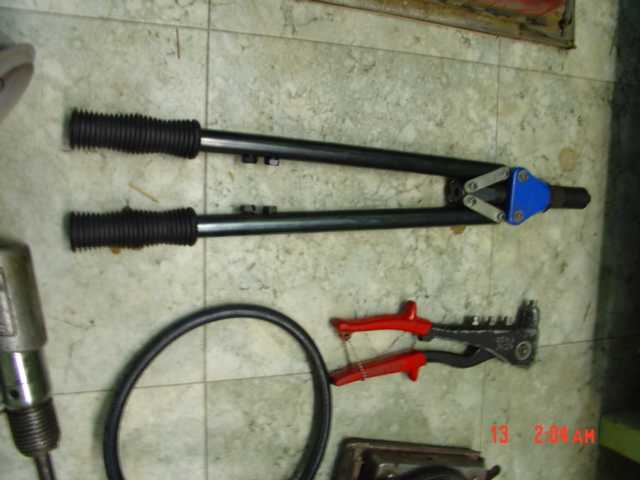 Rivet gun with black handles and blue head, red-handled tool, and black hose on tiled floor