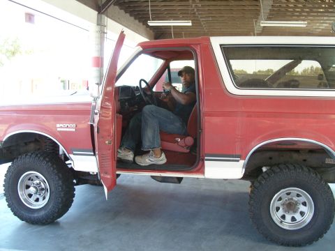 1989 Ford Bronco - A man sits in the driver's seat of a red Ford Bronco with the door open.