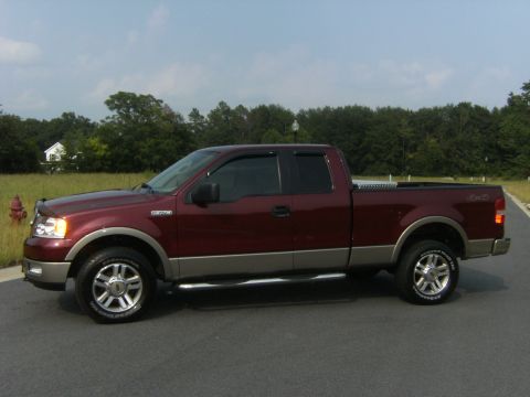 2005 Ford F-150 - Maroon 2005 Ford F-150 pickup truck parked on asphalt with trees and a house in the background.
