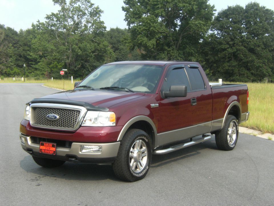 Maroon and tan Ford F-150 pickup truck parked on asphalt, trees and grass in background
