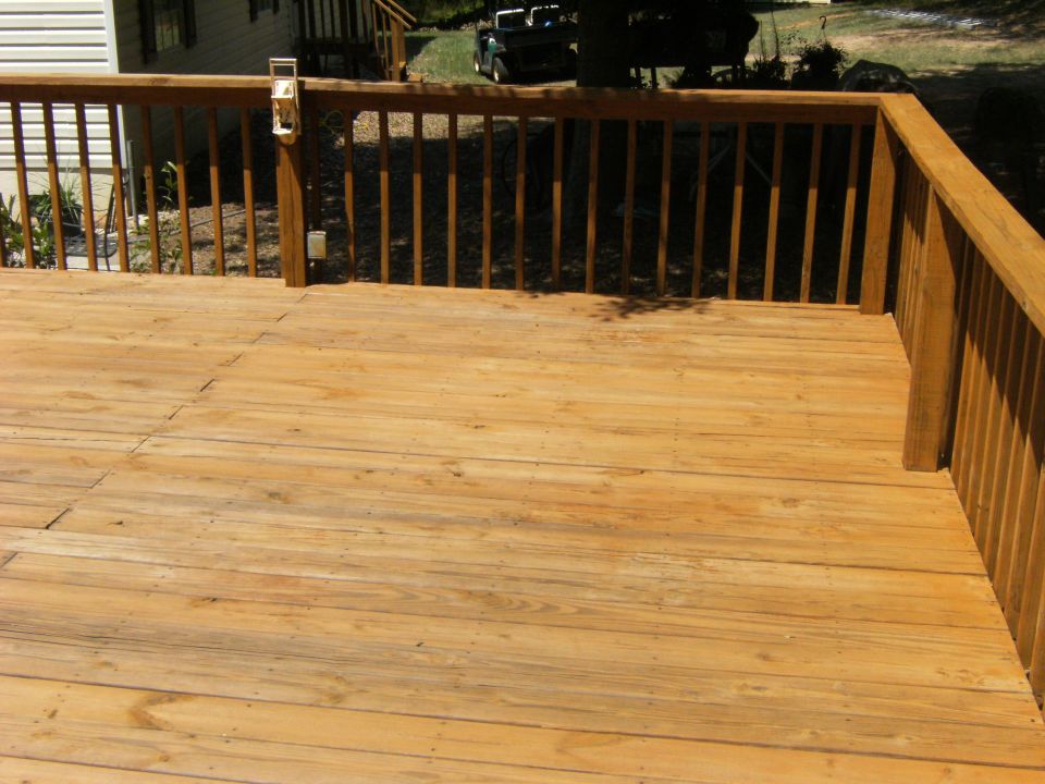 Wooden deck in foreground, house and a dark-colored vehicle in background