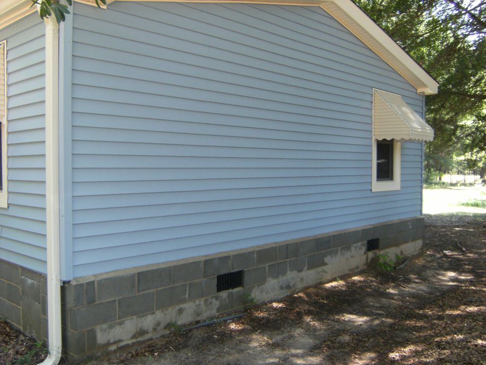 Exterior of a light blue house with a concrete block foundation and a white downspout