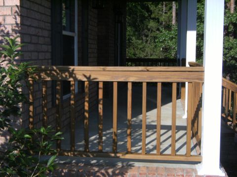 1992 Ford F-150 - Close view of a pressure-treated wood porch railing with square balusters along a concrete porch slab, set against a brick house wall and w…