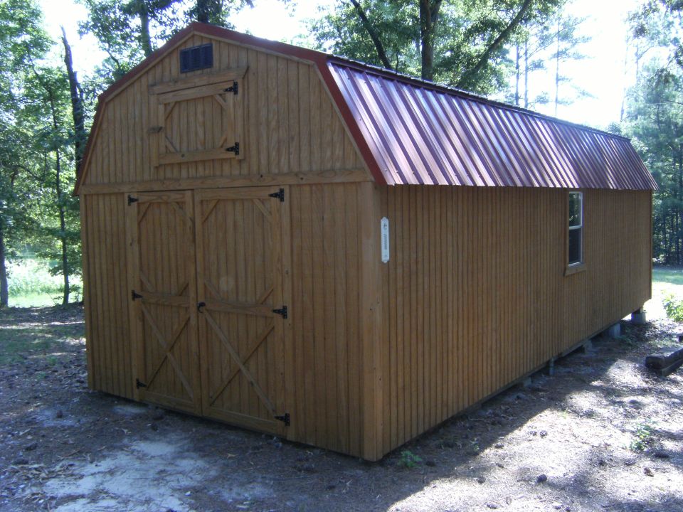 Wooden shed with double doors and a metal roof, set in a wooded area