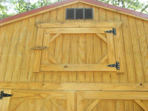 1992 Ford F-150 - Close view of the gable end of a wooden barn-style shed, showing a hinged loft door with black T-strap hinges, a louvered gable vent, red m…
