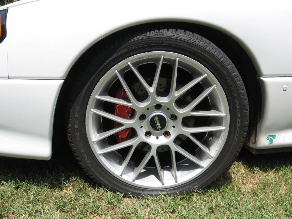 Silver multi-spoke wheel with red brake caliper on a white car
