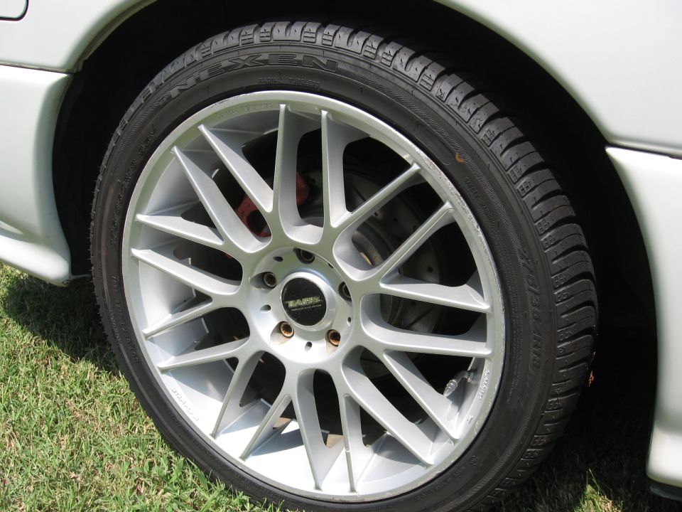 Close-up of a silver multi-spoke aftermarket wheel with a black center cap and red brake caliper visible behind it