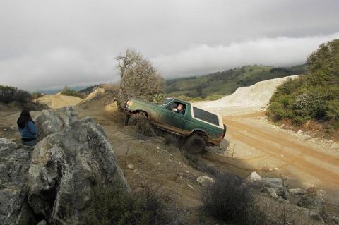1991 Ford Bronco - A green SUV navigates a steep dirt incline with a person watching from the rocks.