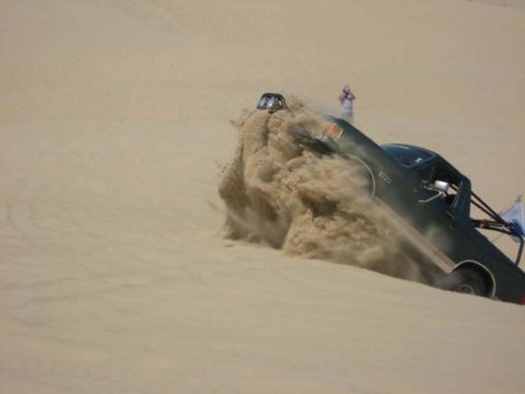 1991 Ford Bronco - A 1991 Ford Bronco navigates a sandy dune, kicking up a large cloud of dust.