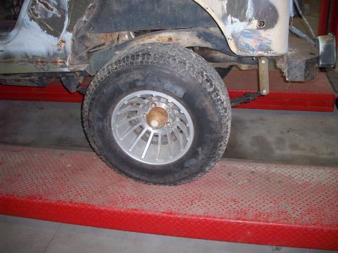 1978 Jeep CJ5 - The side of a Jeep CJ-series vehicle is shown on a red lift, with visible rust and damage to the body panels.