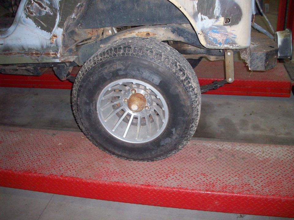 Side view of a Jeep CJ-series vehicle on a red lift. Body shows rust and damage