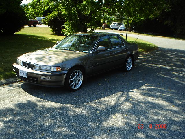 Gray sedan with aftermarket wheels parked on a paved surface under trees