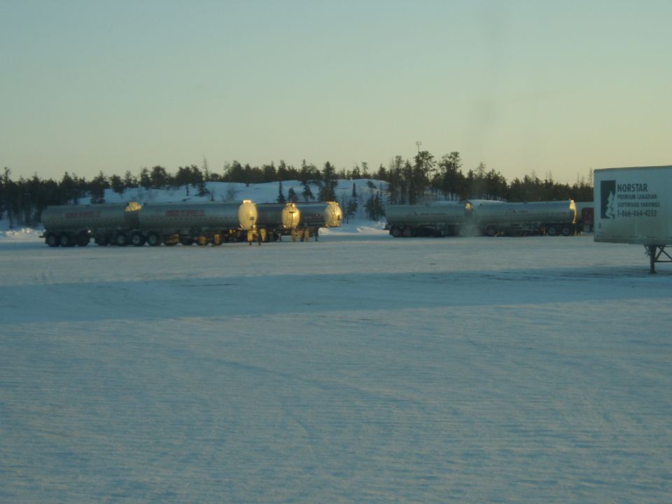 Several tanker trucks parked in a snow-covered field with trees in the background. A Norstar trailer is visible on the right