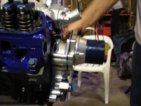 1985 Ford Bronco - A mechanic installs a water pump onto a blue engine block in a workshop setting.