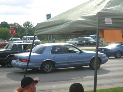 1988 Mercury Grand Marquis - A light blue sedan cruises by, appearing to be from the early 1990s, during a car show.