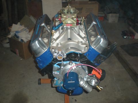 1985 Ford Bronco - A V8 engine with chrome valve covers and blue accents is displayed on an engine stand in a garage setting.