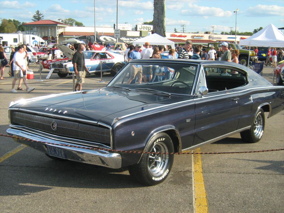Dark blue 1966 Dodge Charger at a car show, front 3/4 view. Other cars and people in background