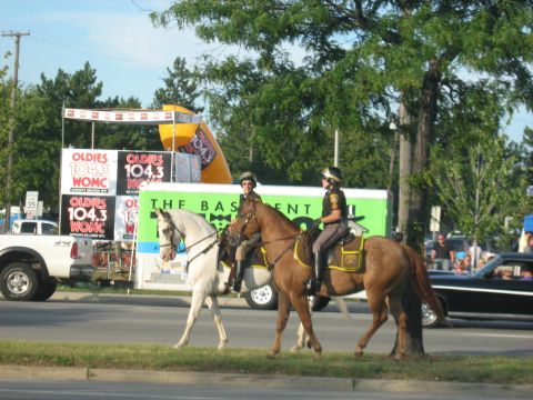 1988 Mercury Grand Marquis - Mounted police officers on horseback patrol during a parade, with a black car and white truck visible in the background.