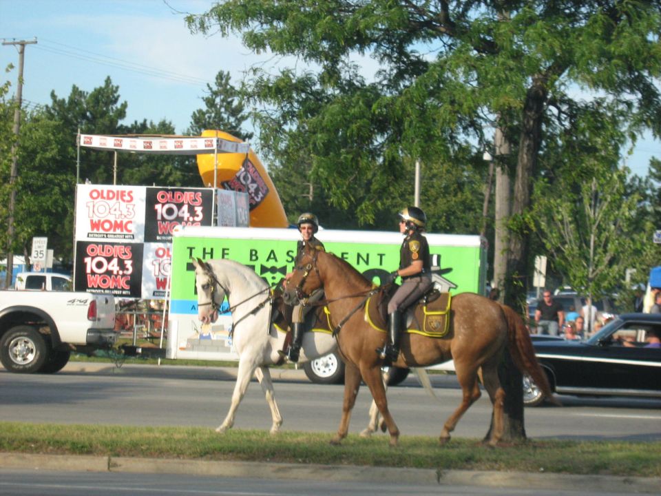 Mounted police officers on horses pass a black car and a white truck