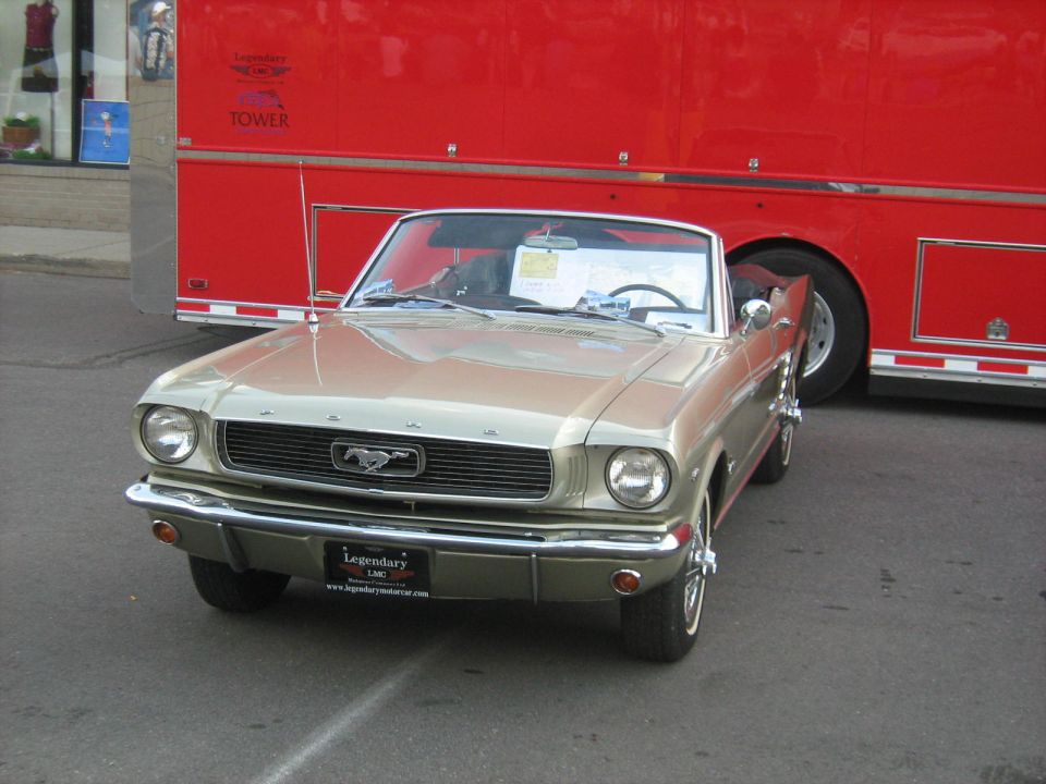 Tan 1965 Ford Mustang convertible parked in front of a red trailer