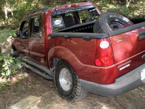 2002 Ford Sport Trac - A red pickup truck is stuck off-road in a wooded area, with its front wheel partially submerged.