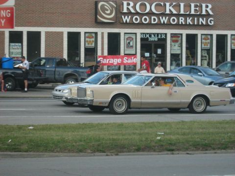 1988 Mercury Grand Marquis - A tan 1977 Lincoln Continental Mark V coupe cruises down the road, passing a garage sale.