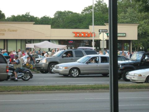 1988 Mercury Grand Marquis - Several vehicles are parked and driving on a street in front of a commercial building.