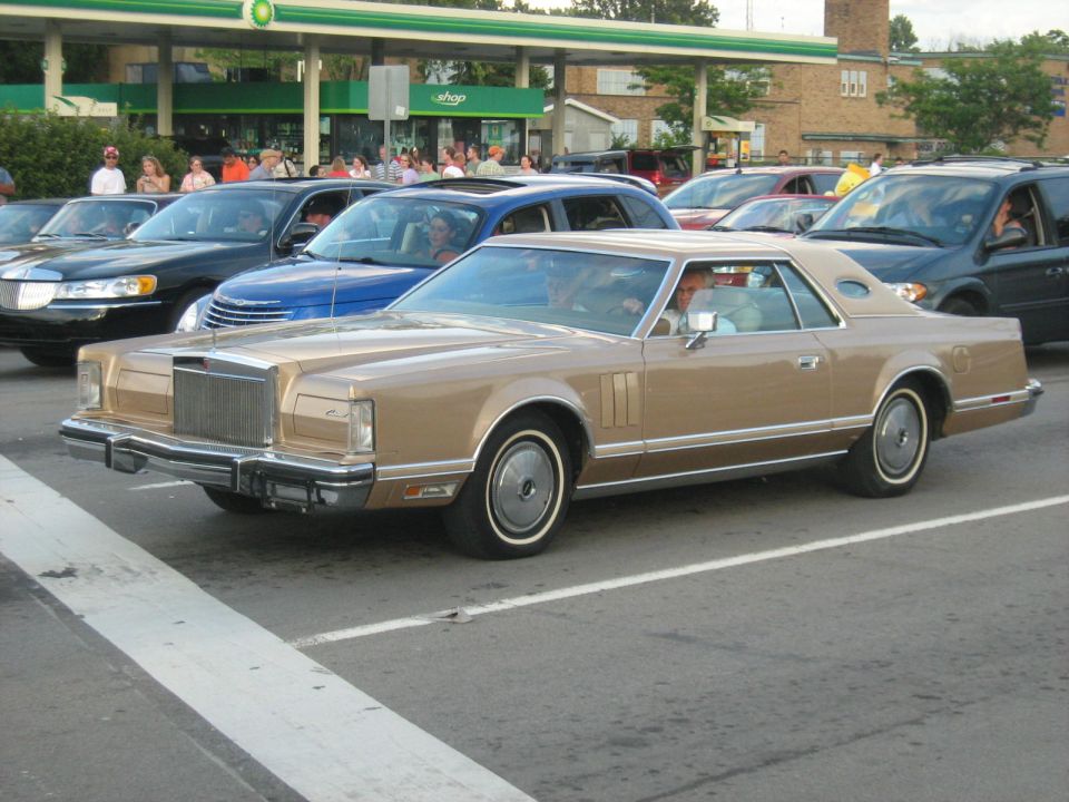 Tan Lincoln Continental Mark V coupe parked in line with other cars at a gas station