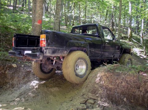 2002 Ford Sport Trac - A black pickup truck with large tires maneuvers through a challenging off-road course in a wooded area.