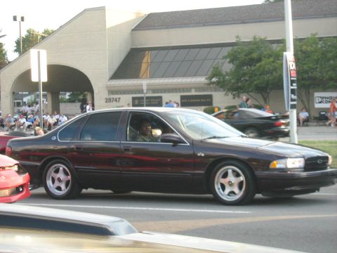 1988 Mercury Grand Marquis - A dark sedan drives past a building with people watching.