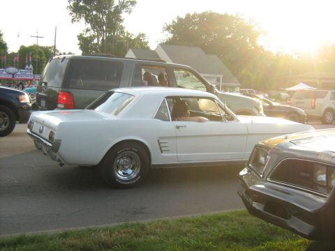 1988 Mercury Grand Marquis - A white 1965 Ford Mustang coupe is seen from the side, with other cars and an SUV in the background.