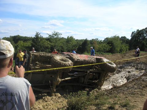 2002 Ford Sport Trac - A vehicle is stuck and overturned in a muddy off-road course, with spectators observing the scene.