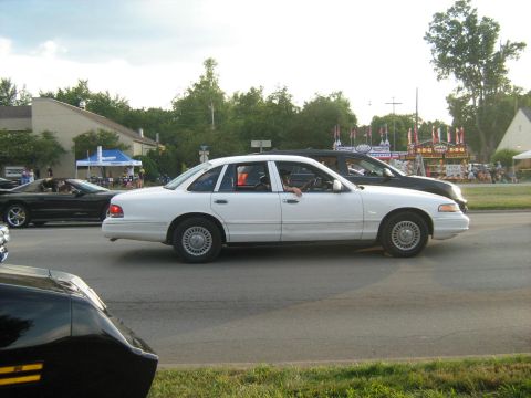 1988 Mercury Grand Marquis - A white sedan drives down a street with a black SUV following closely behind.