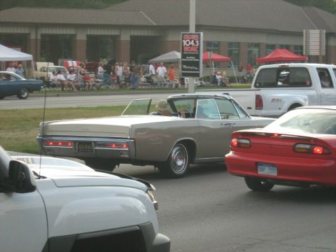 1988 Mercury Grand Marquis - A tan convertible cruises down the road during a car show, with other vehicles and spectators visible.