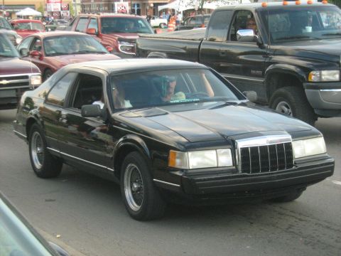 1988 Mercury Grand Marquis - A black Lincoln Mark VII is seen in traffic, with several other vehicles visible.