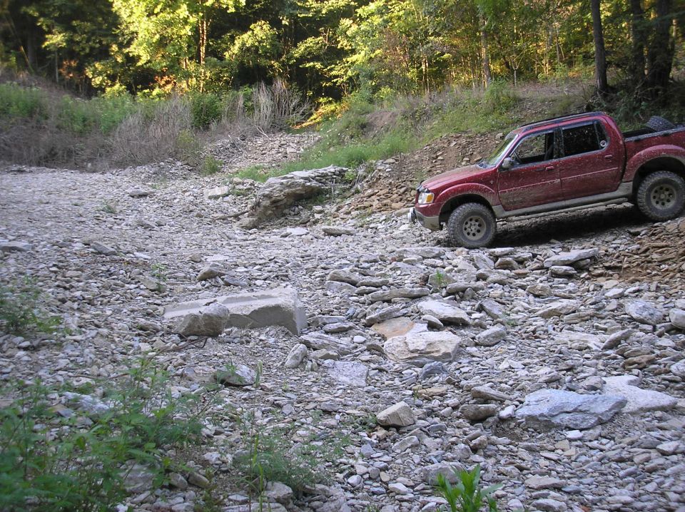 Red 2002 Ford Sport Trac driving on a rocky, wooded trail