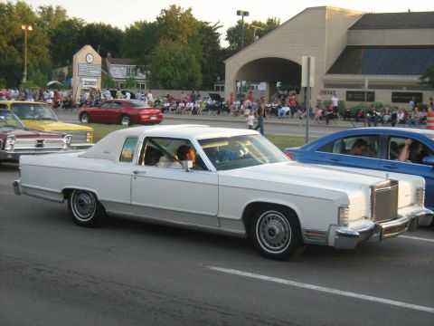 1988 Mercury Grand Marquis - A white sedan cruises down the street during a parade, with spectators lining the sidewalks.