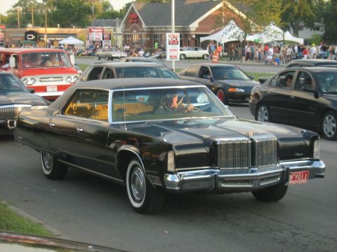 1988 Mercury Grand Marquis - A classic black sedan cruises down the street, its chrome grille and whitewall tires catching the light.