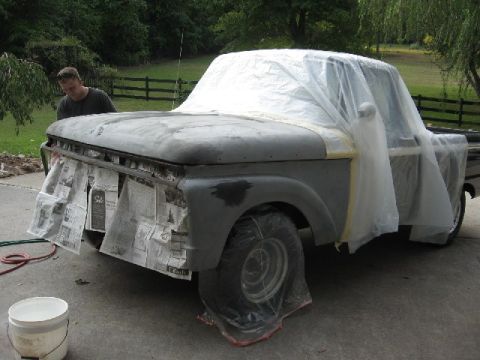 1966 Ford F-100 - Man preps 1966 Ford F-100 for paint, covering the front end with plastic and newspaper.
