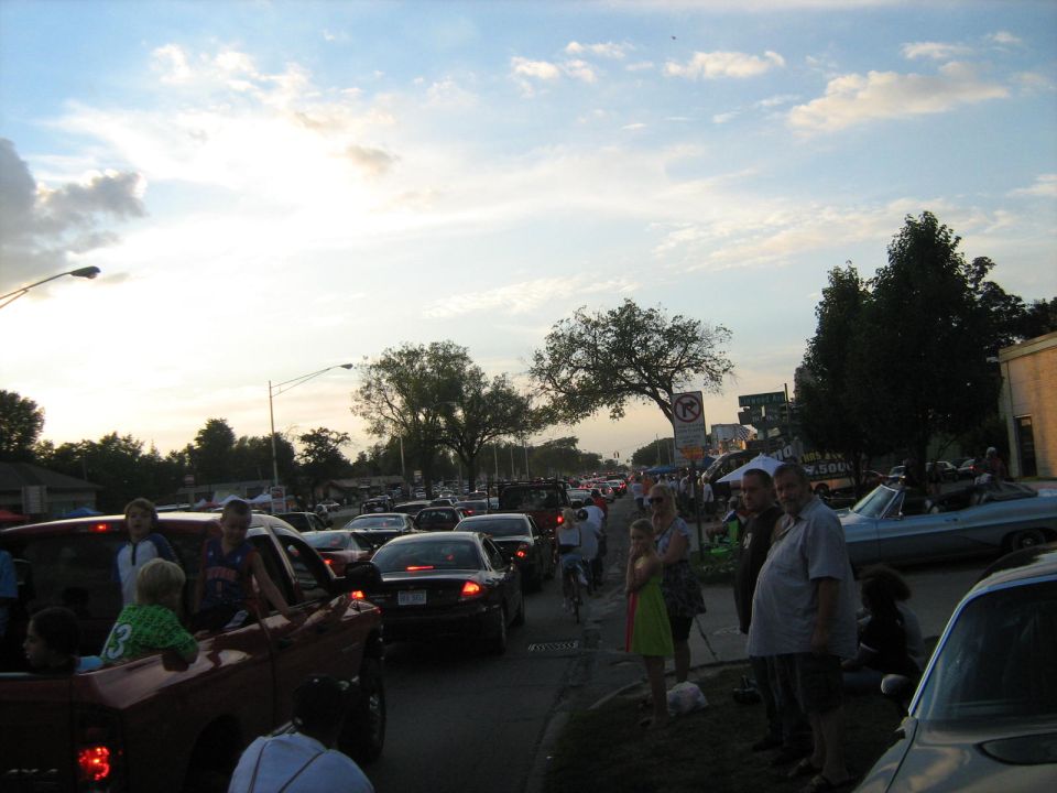 Cars backed up on a street with people standing on the side, some in a pickup truck bed
