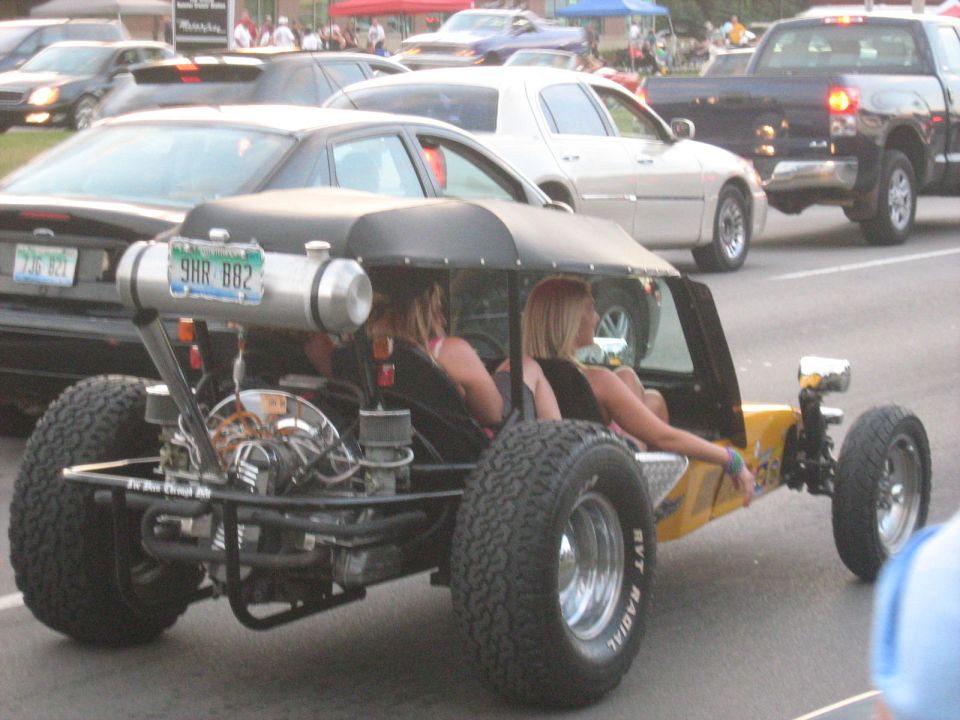 Yellow dune buggy with exposed engine and large rear tires, carrying two passengers
