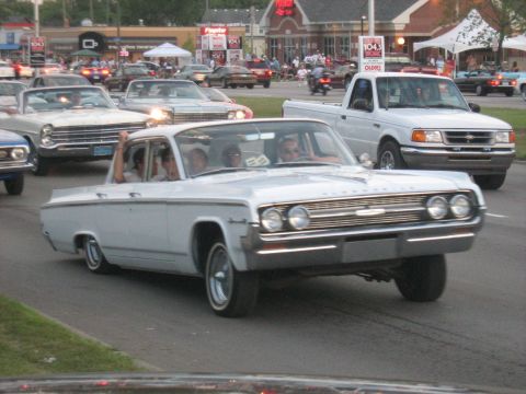 1988 Mercury Grand Marquis - A white sedan cruises down a street with other cars and buildings in the background.