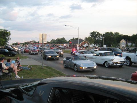 1988 Mercury Grand Marquis - A silver convertible sports car is seen during a cruise event with many other vehicles on the road.